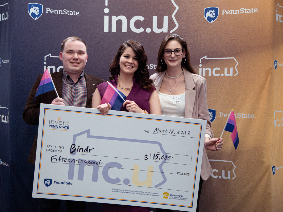 Three founders stand against Inc.U backdrop holding oversized check for $15,000