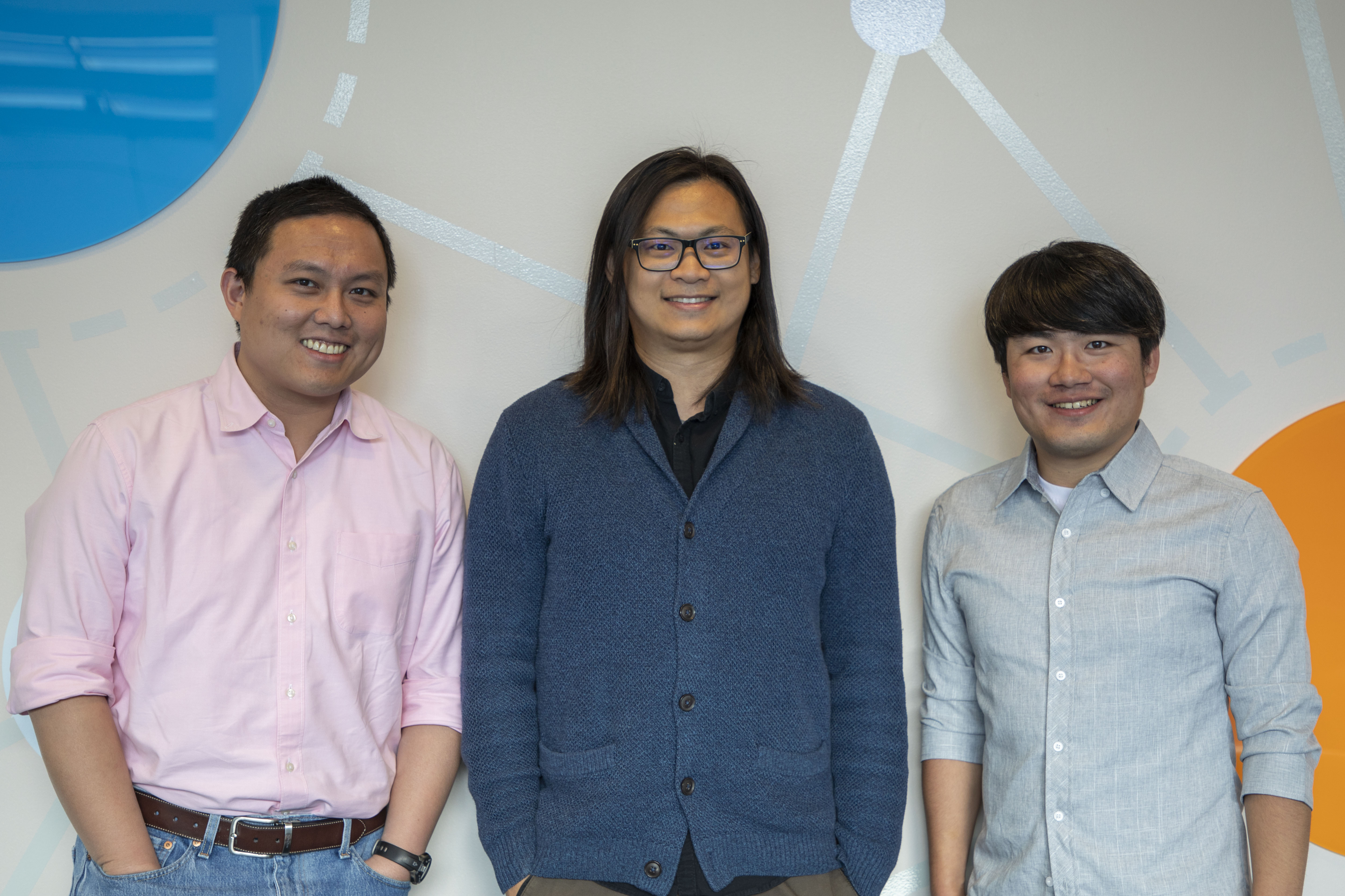 Three smiling people standing against a colorful wall