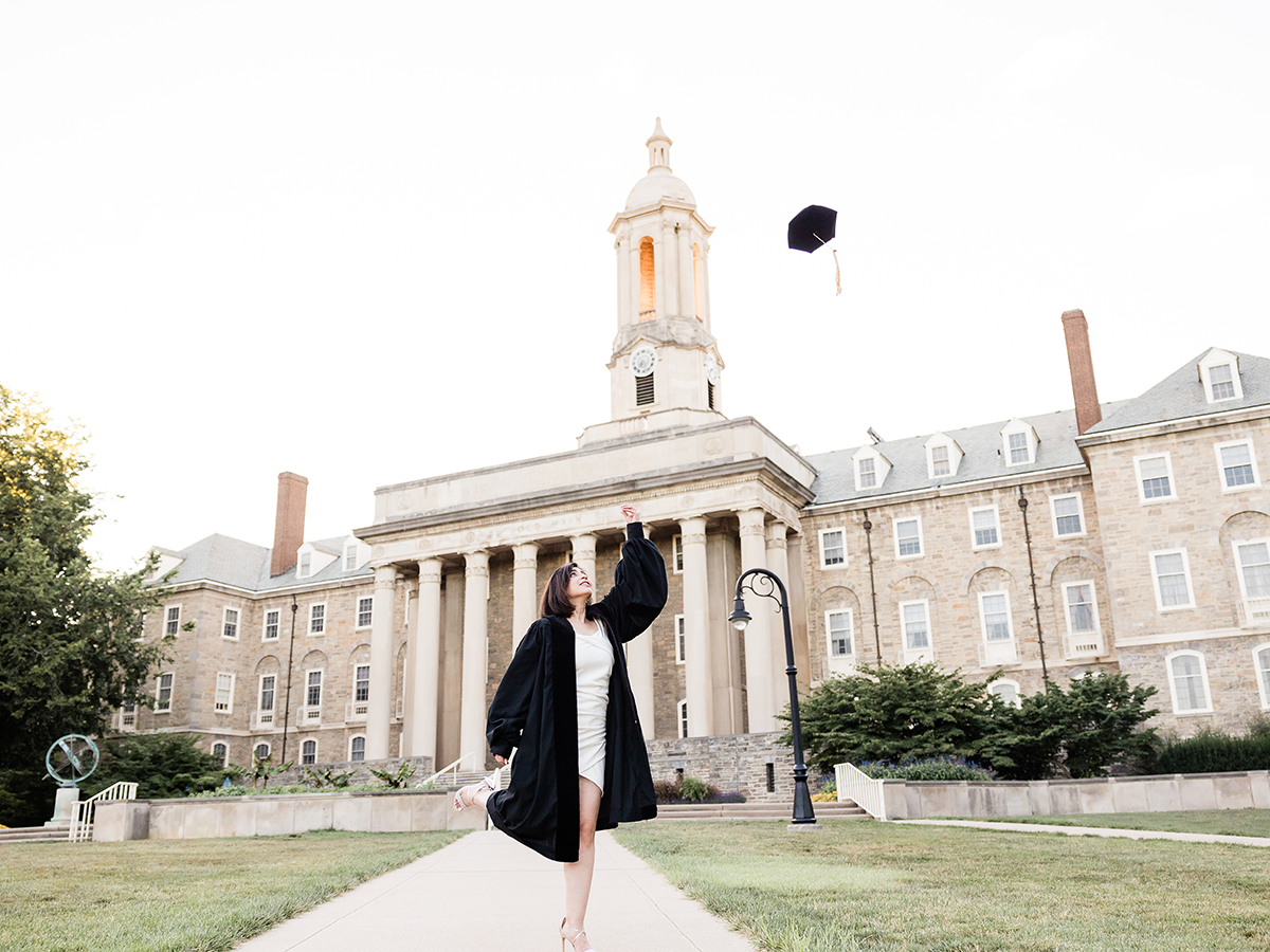 Mahda Bagher wearing a graduation gown and tossing her tam into the air in front of the Old Main building