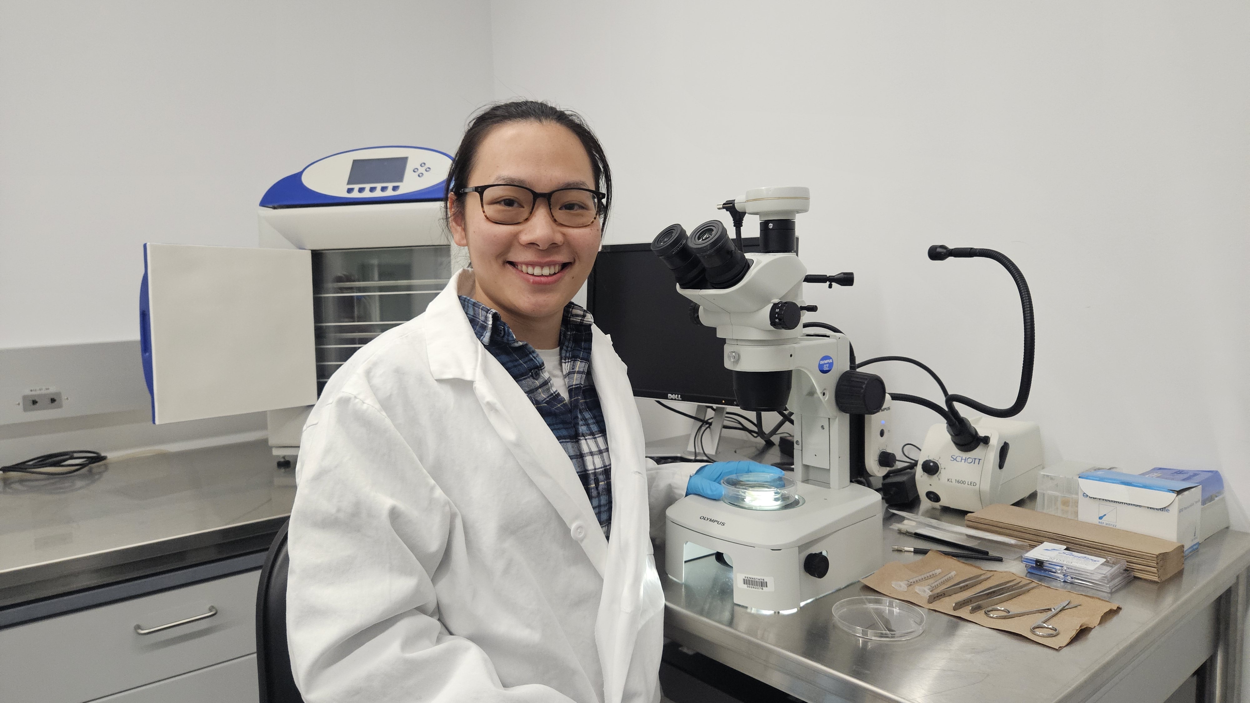 Person wearing a lab coat standing in front of a microscope