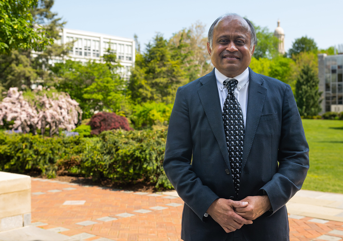 A person in a suit and tie stands outside and smiles at the camera