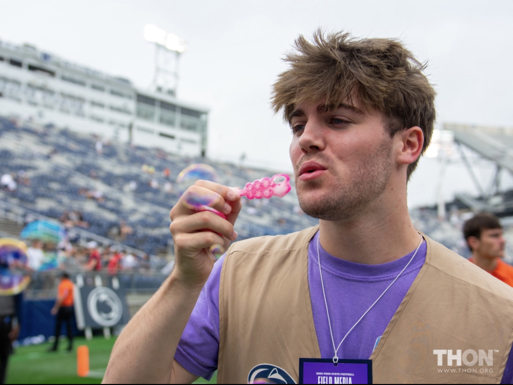 A person blowing bubbles on a football field. Stands visible in the background.