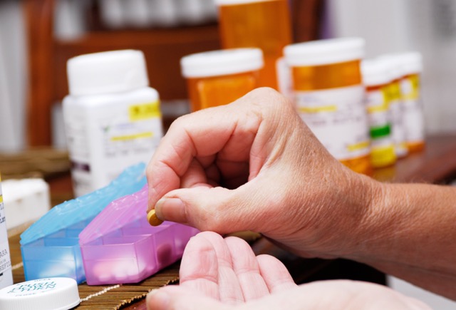 A woman’s hand shown filling pill boxes, with prescription bottles in the background.