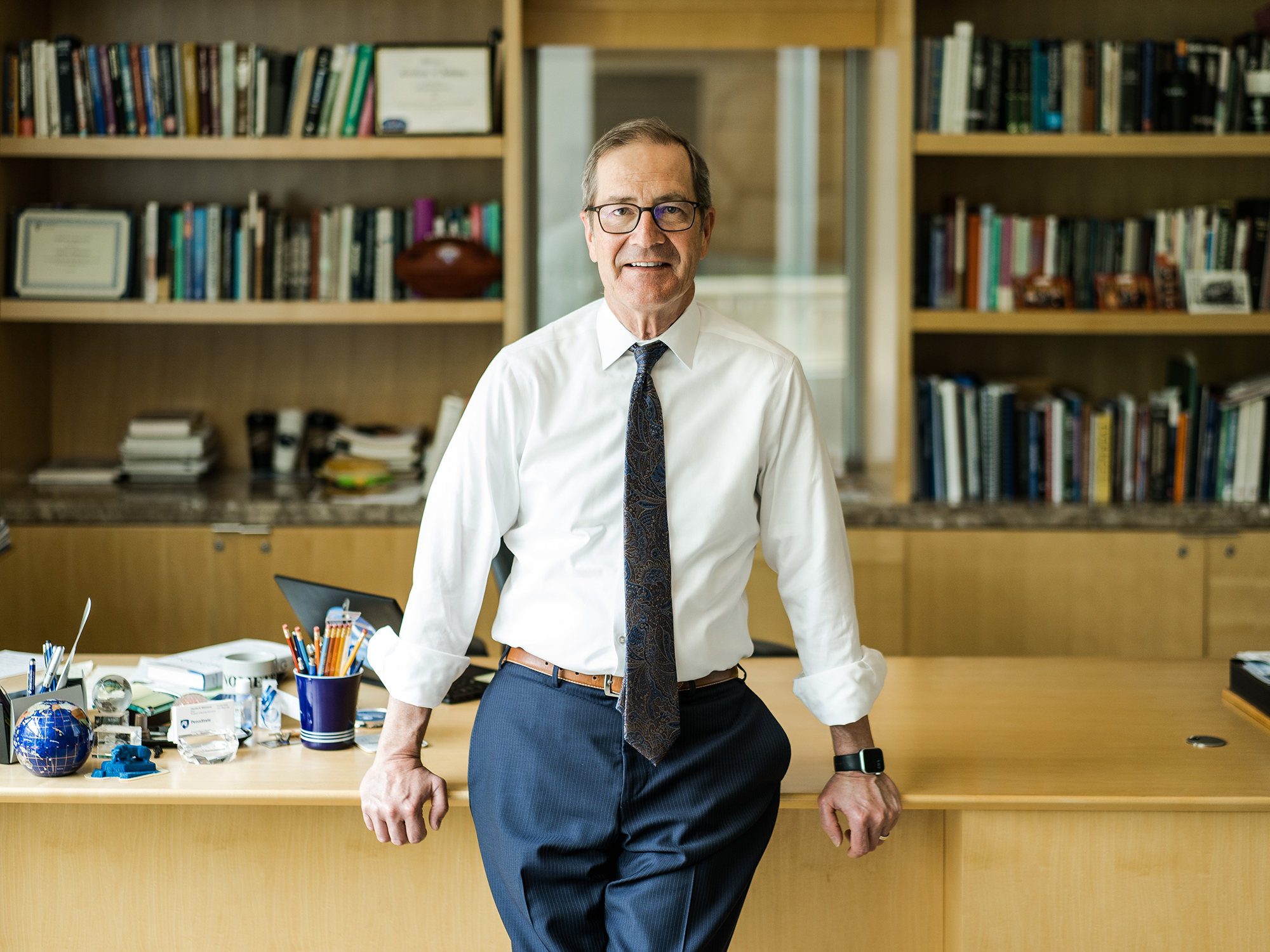 Smeal College of Business Dean Charles Whiteman leaning against a desk with bookshelves behind him. 