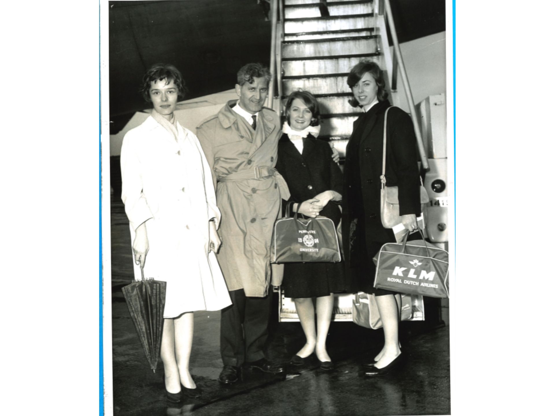 Three young women and a young man stand at the bottom of stairs leading to an airplane