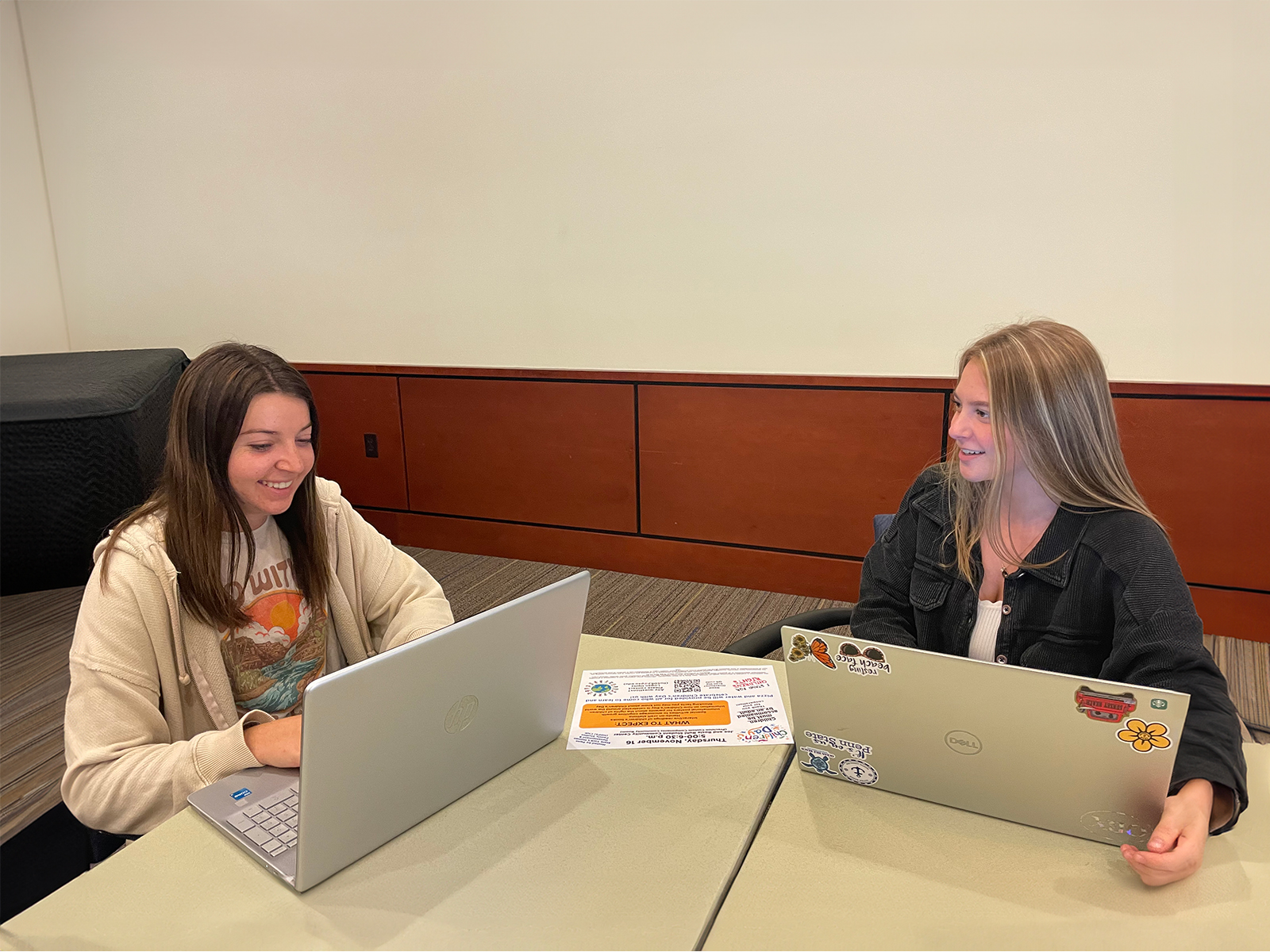 Two female students with long hair working at laptops at a table