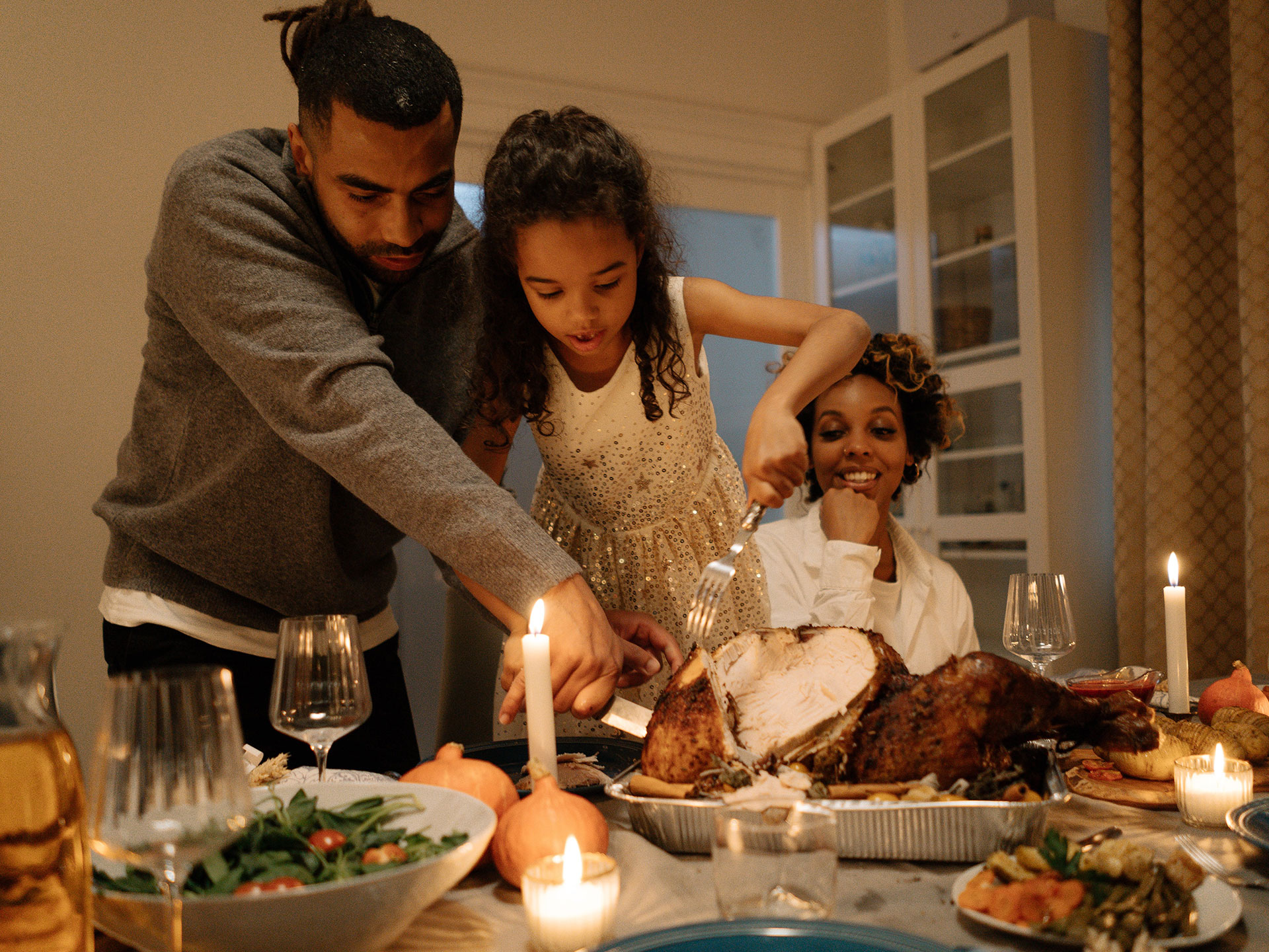 Father, child, mother carve a turkey at Thanksgiving