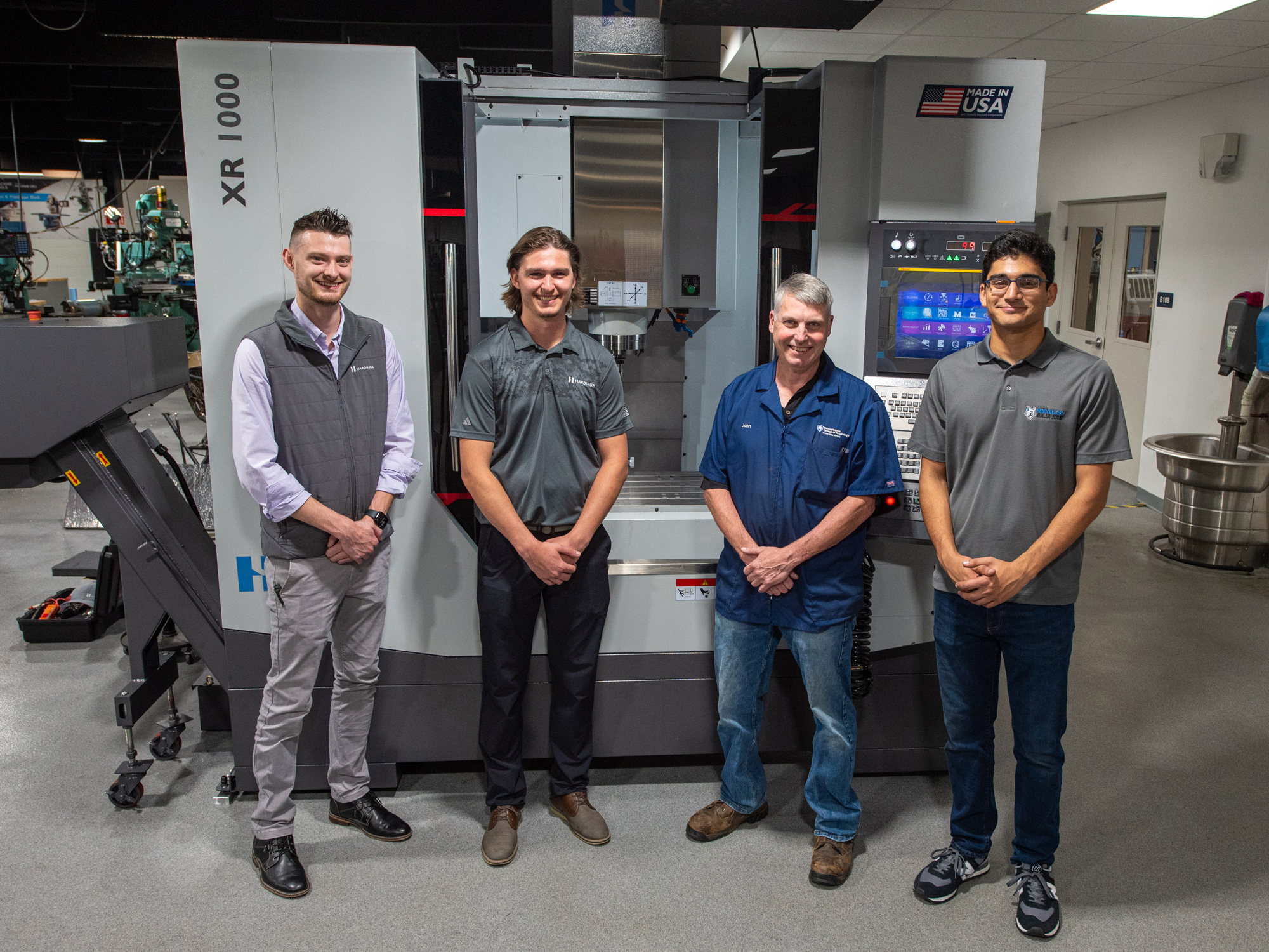 Four people stand in front of a vertical machining center