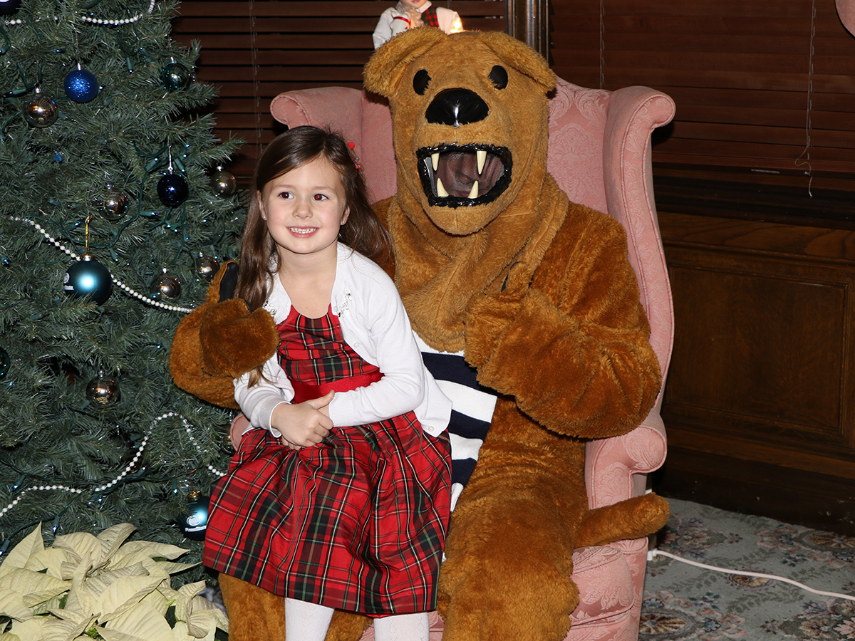 A child and the Nittany Lion pose near a Christmas tree.