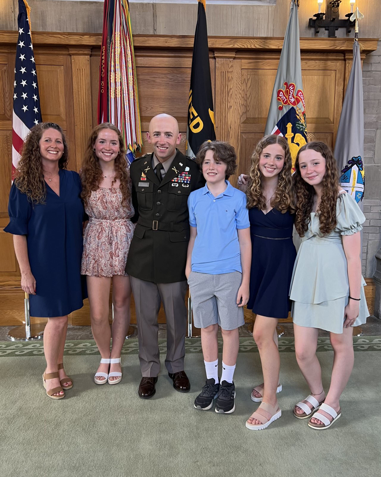 Six people pose together in front of flags.