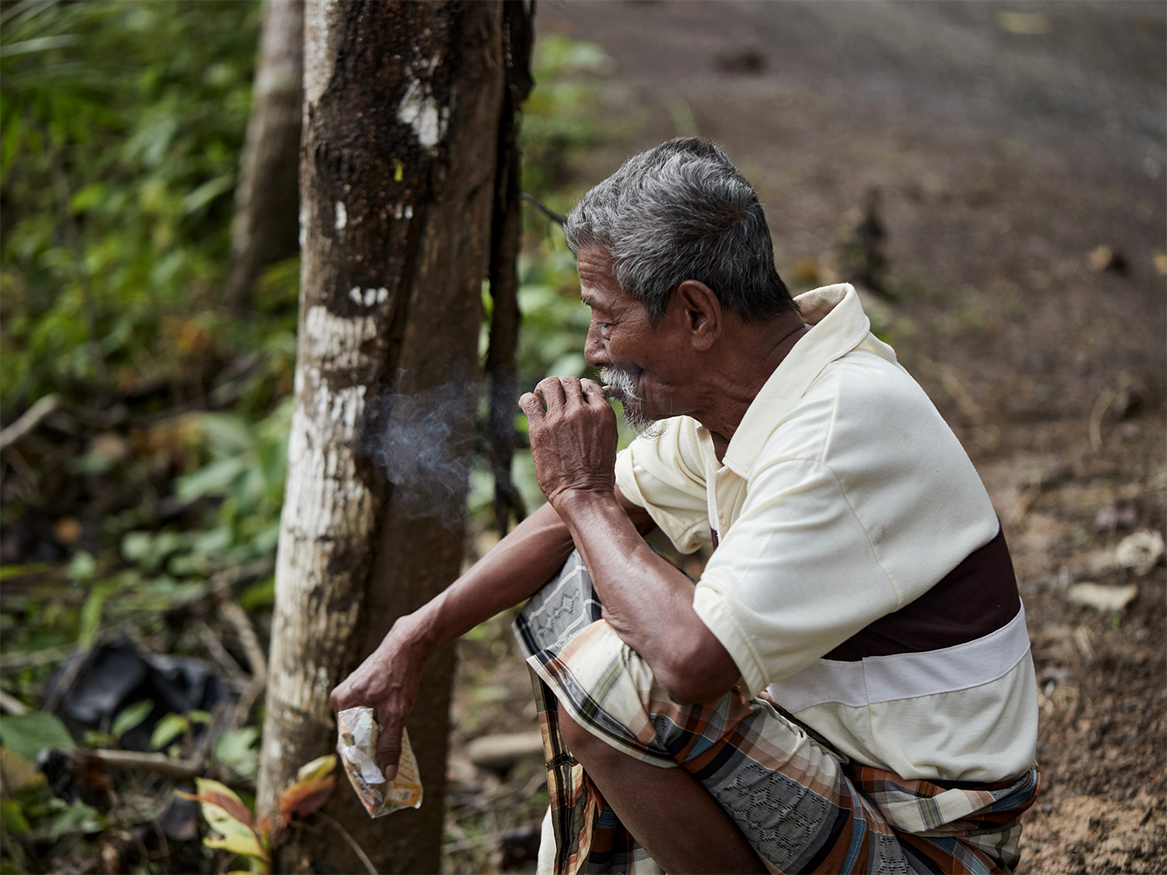 Man squatting by side of dirt road and smoking