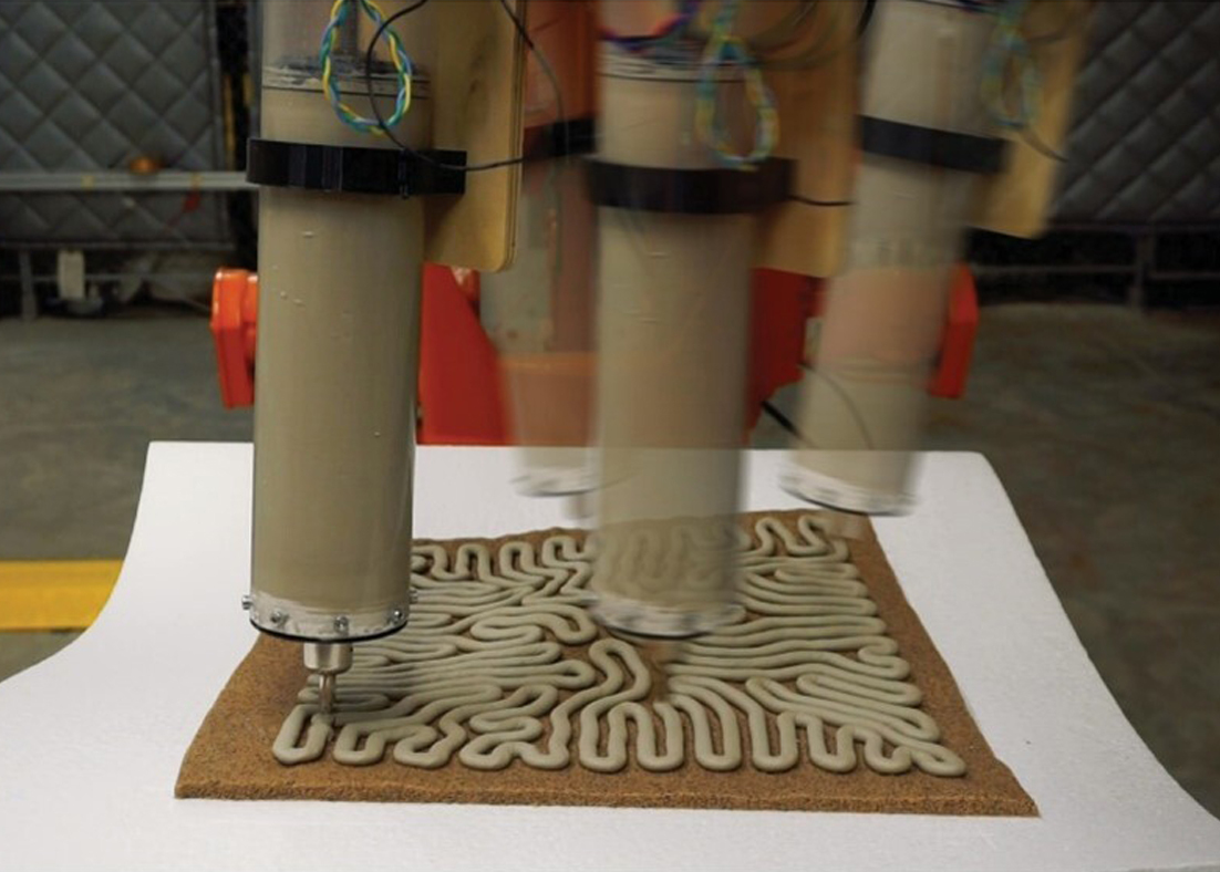 A time-lapse image showing a robotic arm extruding a concrete substance as it 3D prints a structure. 