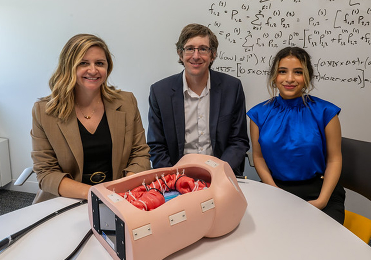 Scarlett Miller, Jason Moore and Isra Elsaadany sit at a table with a manikin on it. 