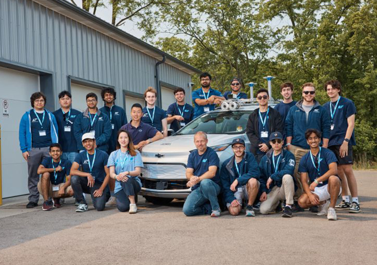 Team members pose for a picture with their autonomous vehicle in front of a garage