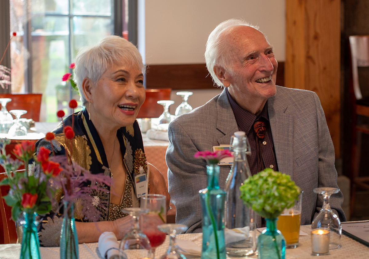 Two smiling individuals sit at a table in a restaurant.