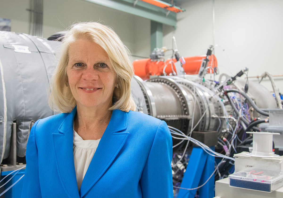 An indoor portrait of an individual standing in front of a gas turbine. 