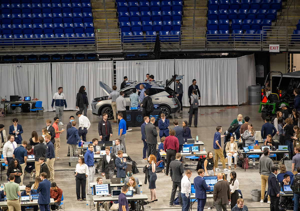 Students walk around tables and a car that are on the floor of the Bryce Jordan Center.