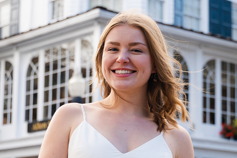 Red-haired young woman in a white sun dress smiling outside. 