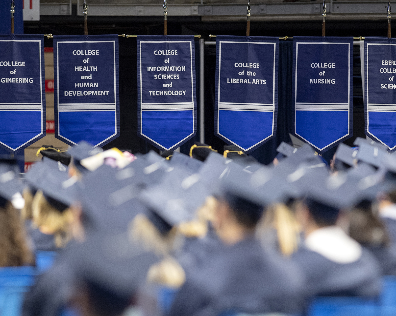 A group of people wear blue graduation caps and gowns during a ceremony.