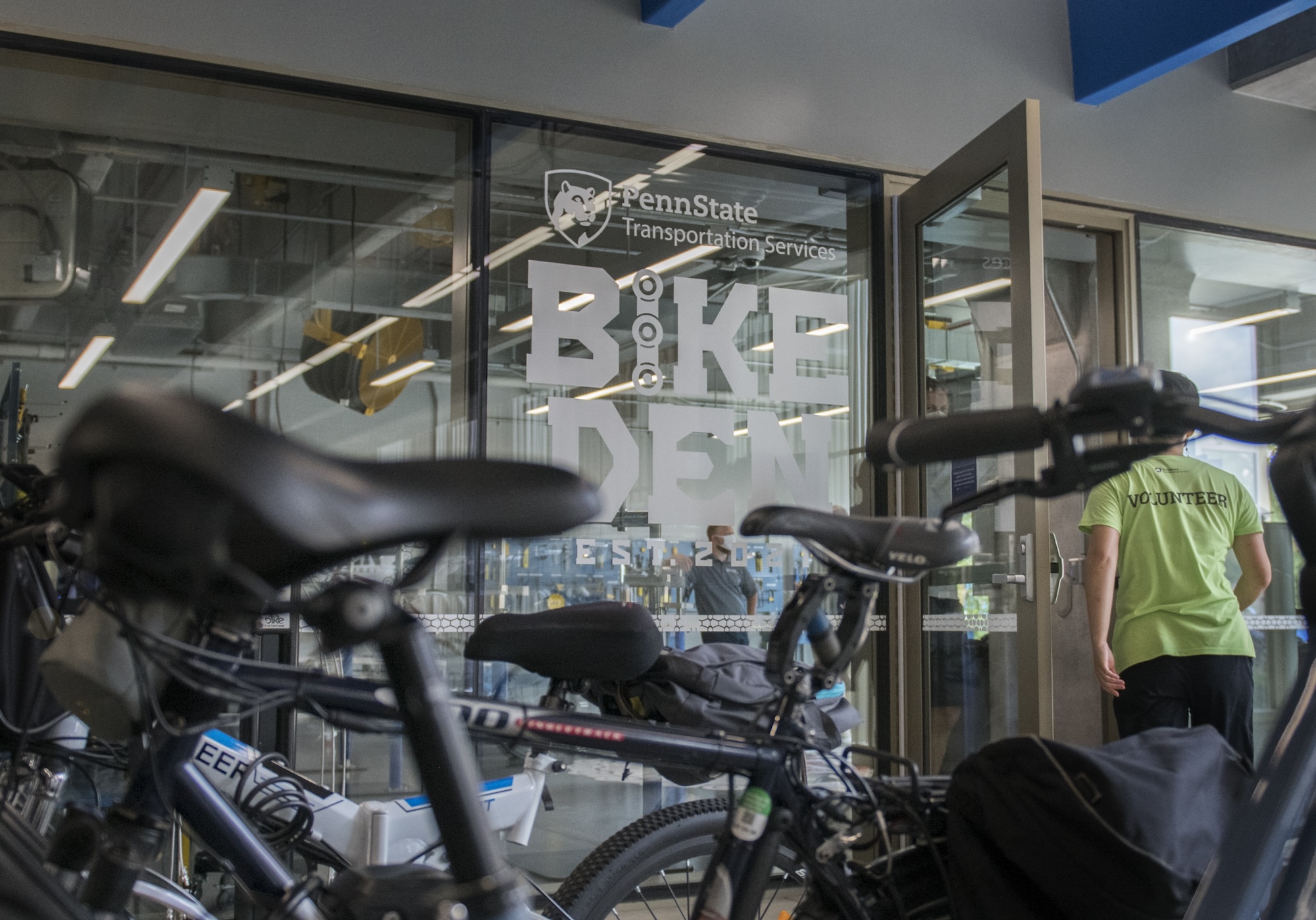 Rows of bikes outside the Bike Den. A person wearing a yellow shirt is walking in the door.