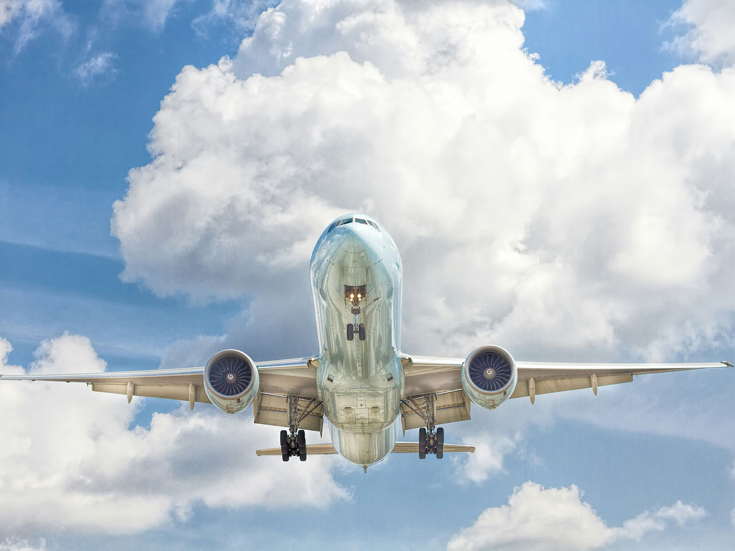 A grey and white airplane in flight in a blue sky with puffy white clouds