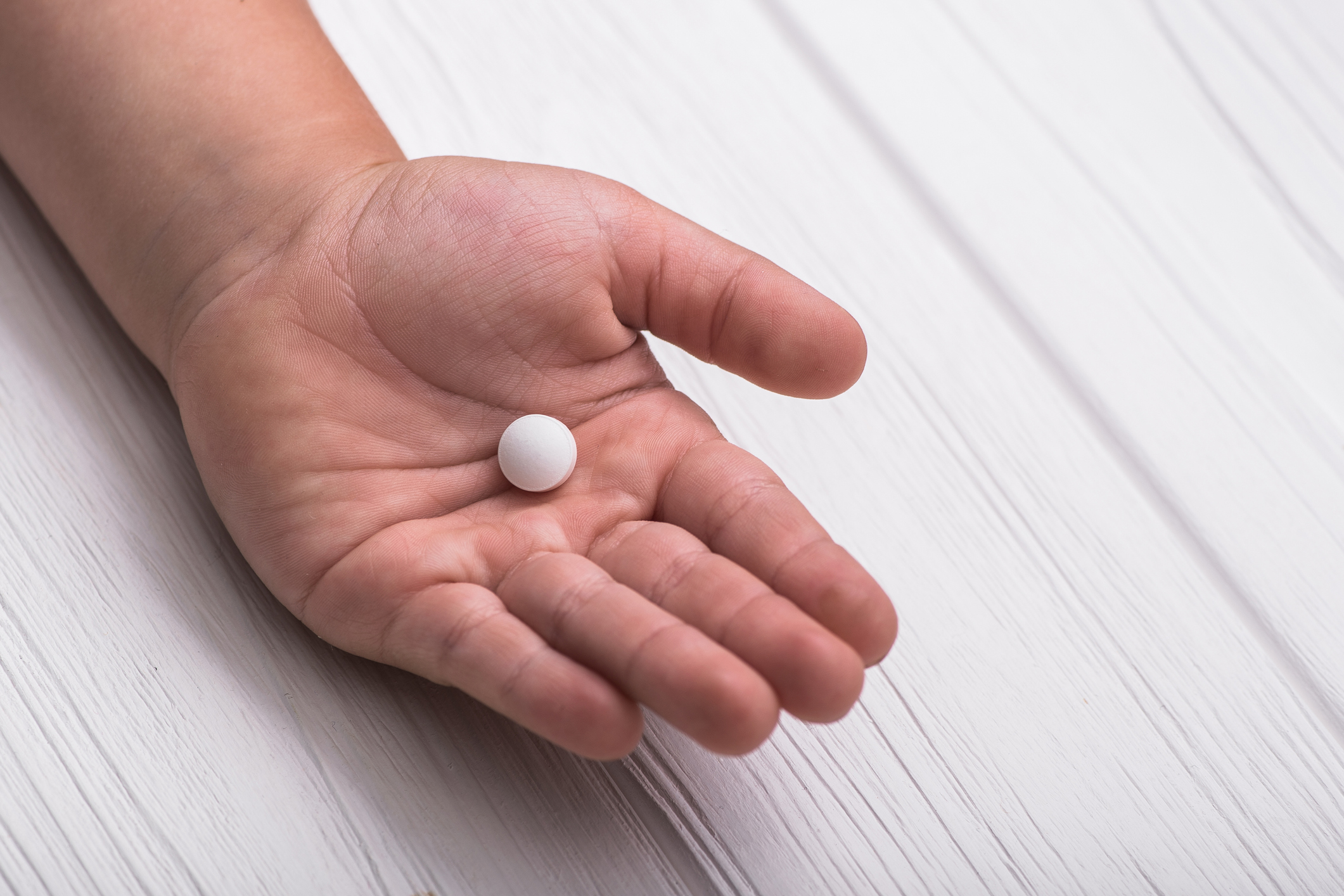 A child's hand holds a white pill