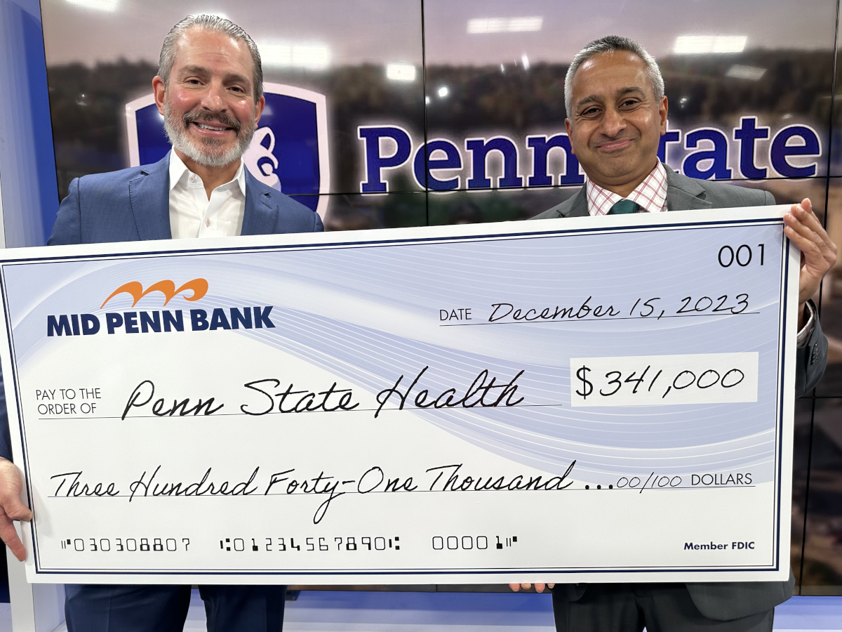 Two men pose for a photo with an oversized check in the amount of $341,000. A large Penn State Health logo is in the background.