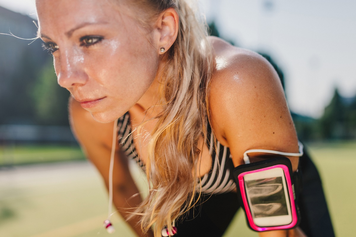 Sweaty, blond-haired woman resting after a hard workout on a sports field.