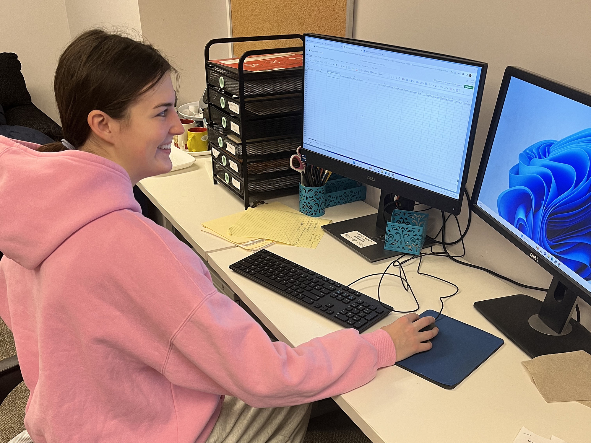 Person sits at desk with two monitors. 