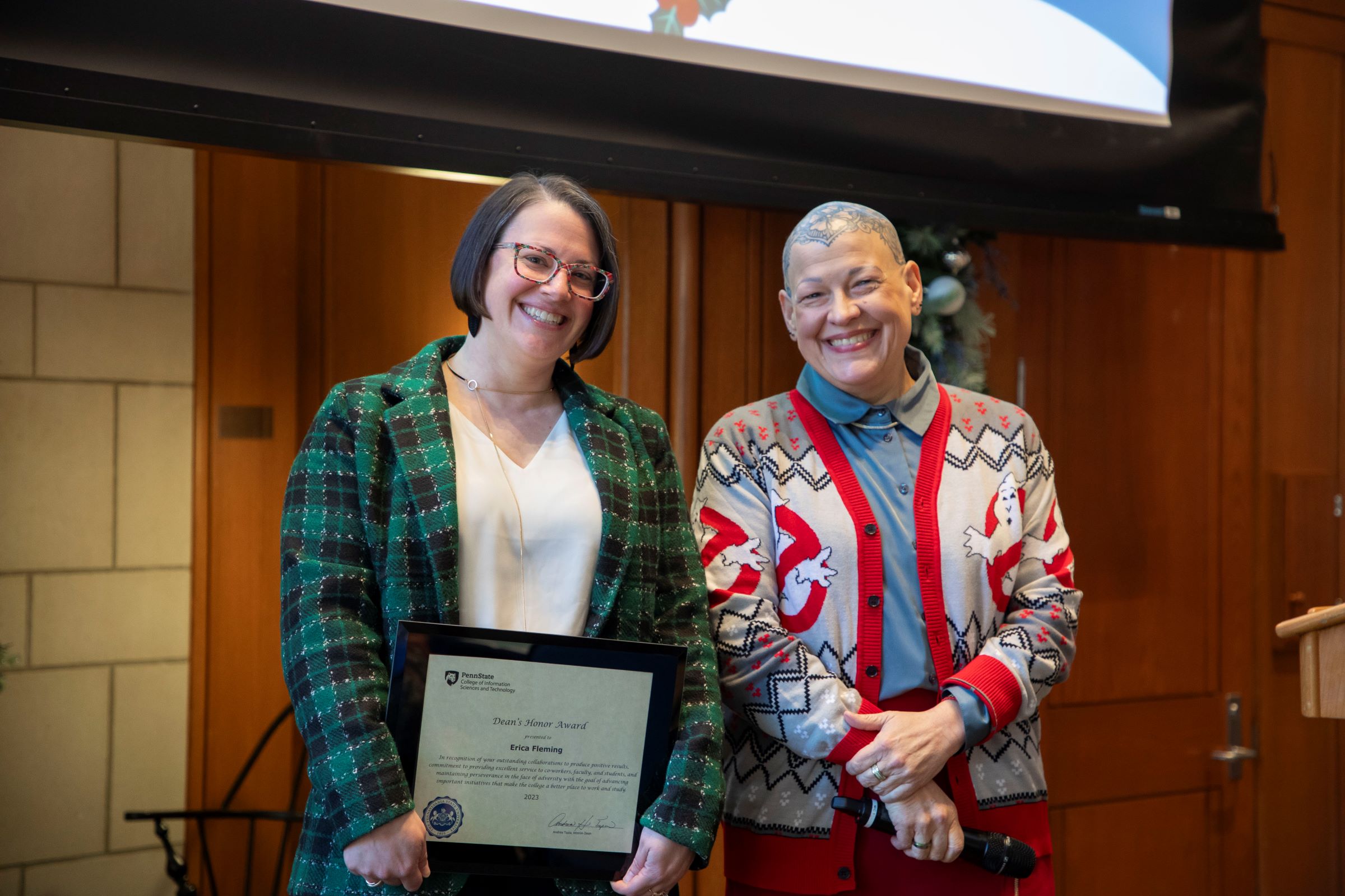 two smiling people display award certificate