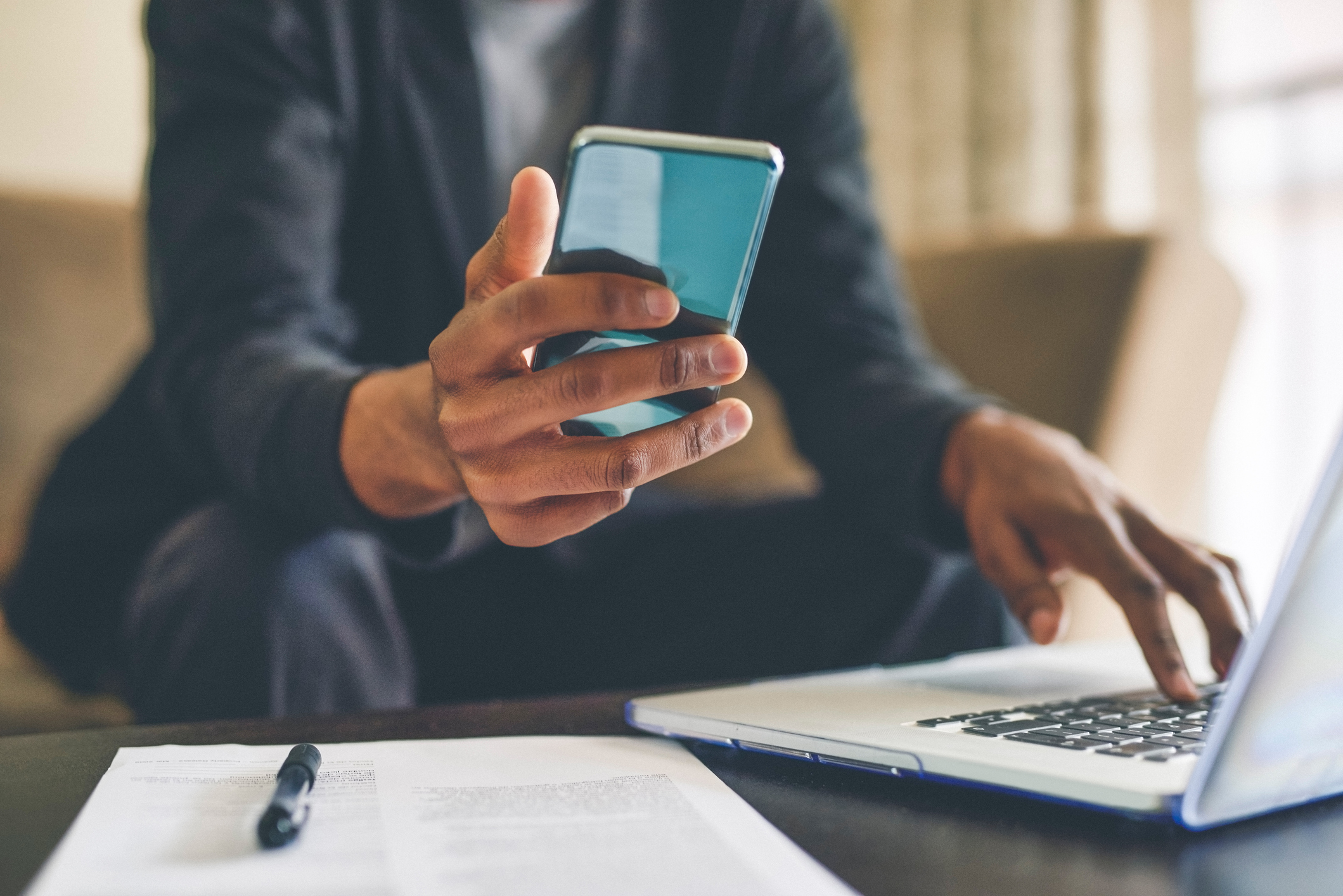 A man looks at his smartphone as he works on a laptop