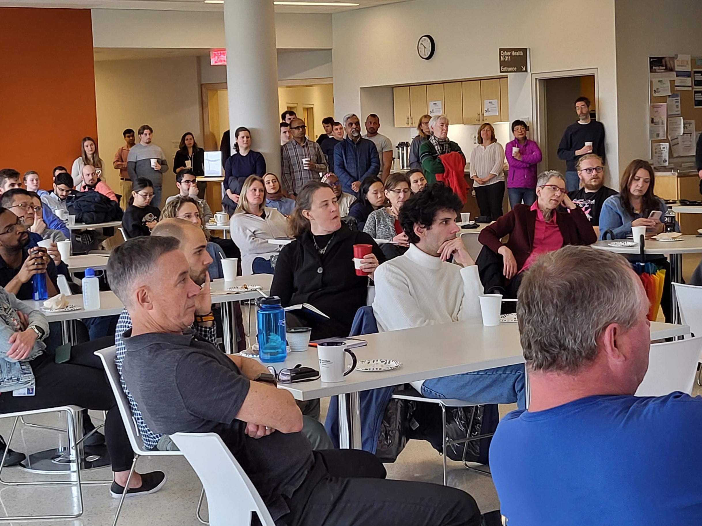 large group of people listening to a talk in a sunny room