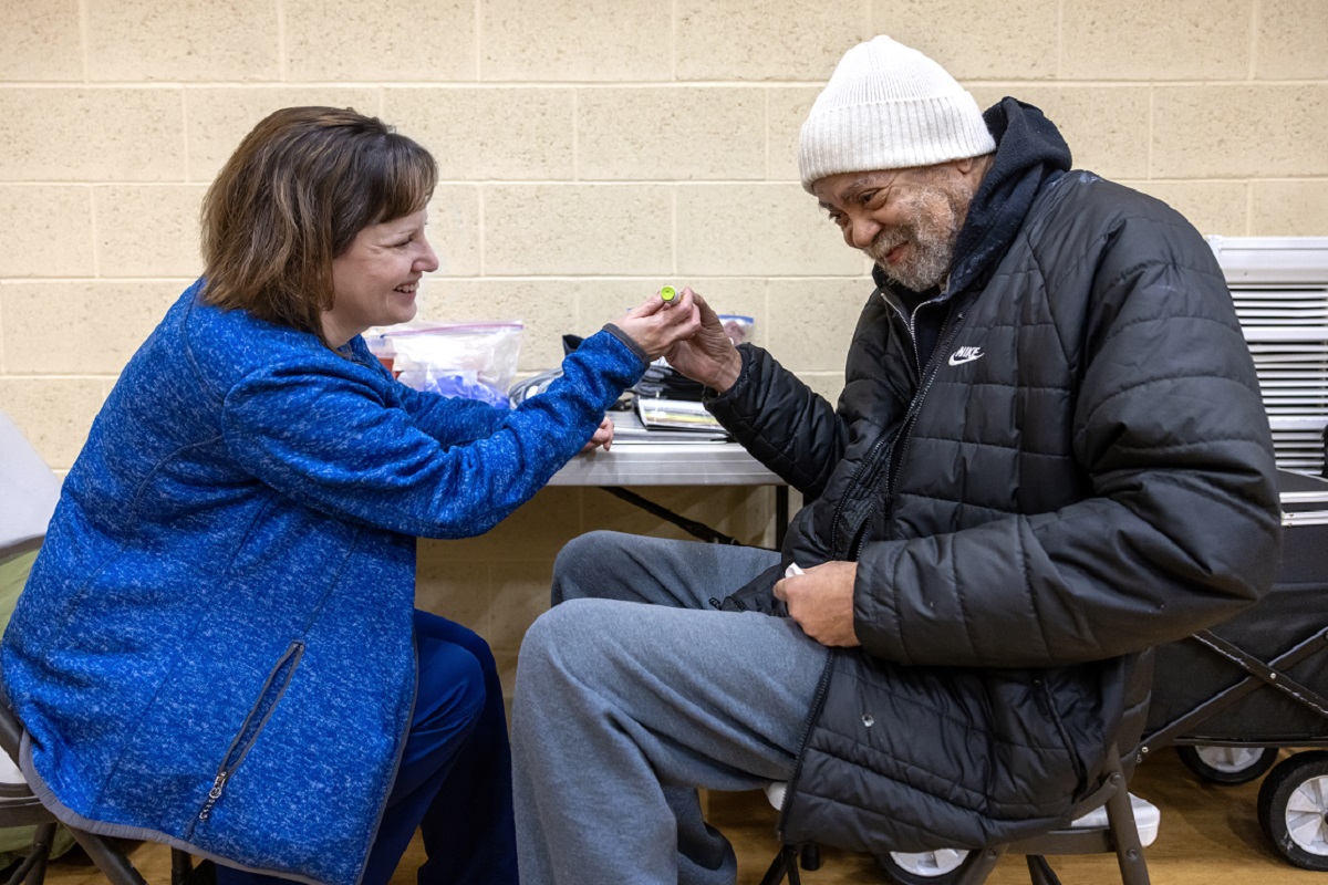 A man in a coat and winter cap reaches across a table and touches the hand of a woman in a coat. Both smile at one another.