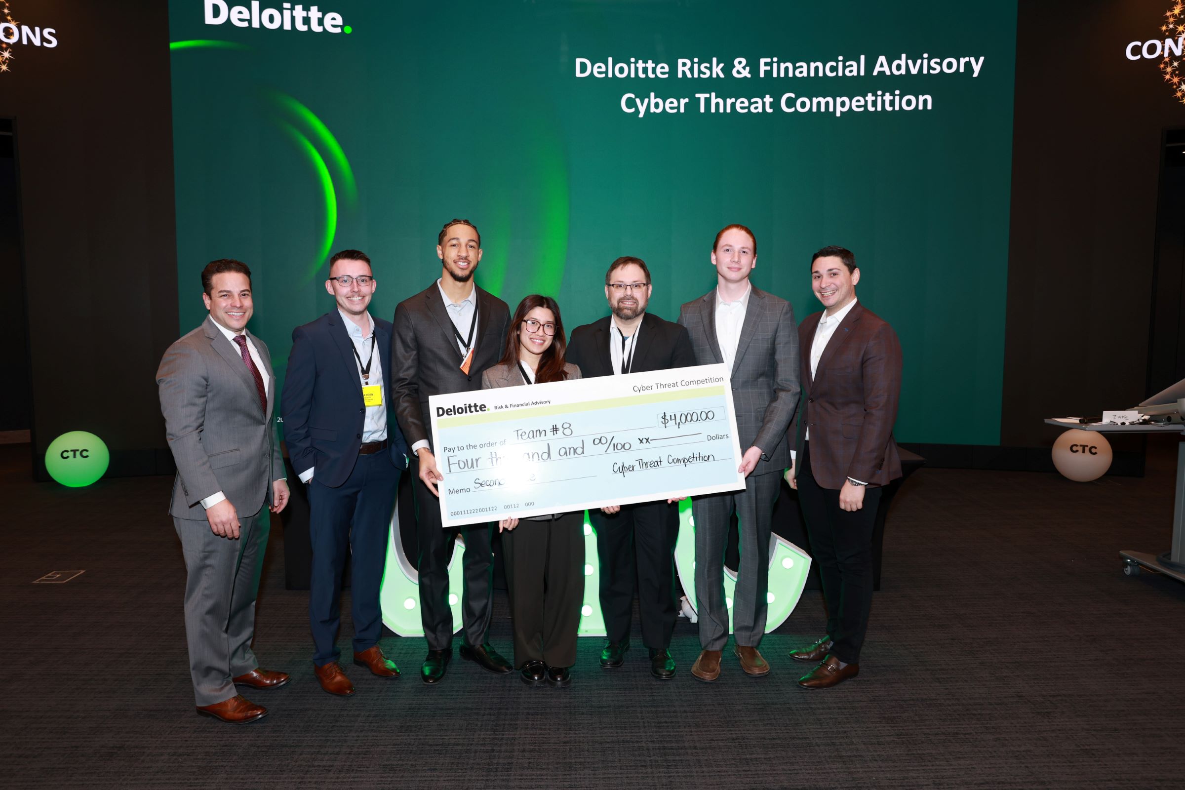 group of people in suits holding giant check against conference backdrop