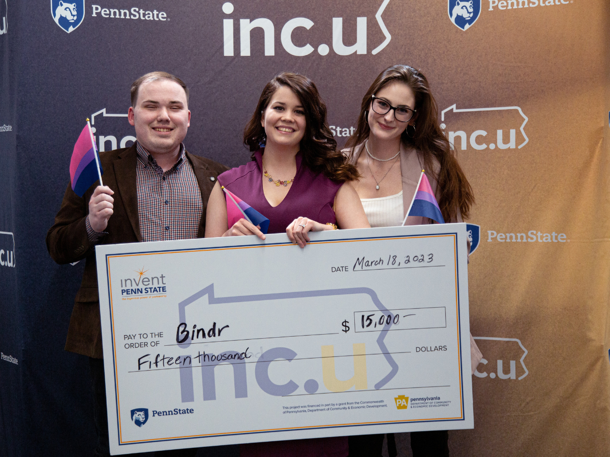 Three individuals hold an oversized check for $15,000 in front of an Inc.U banner