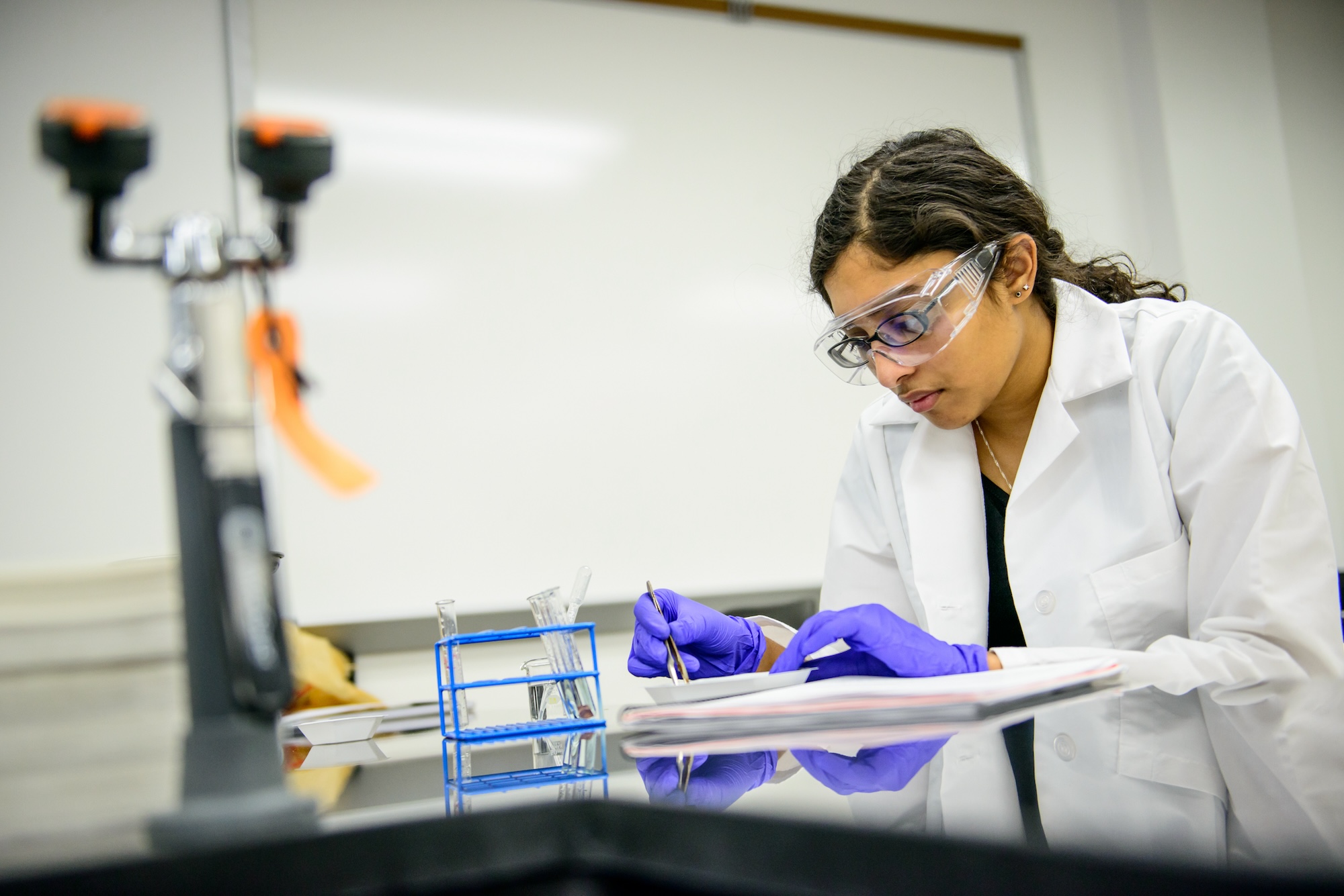 Individual performing laboratory experiment with white lab coat, safety glasses, and gloves.