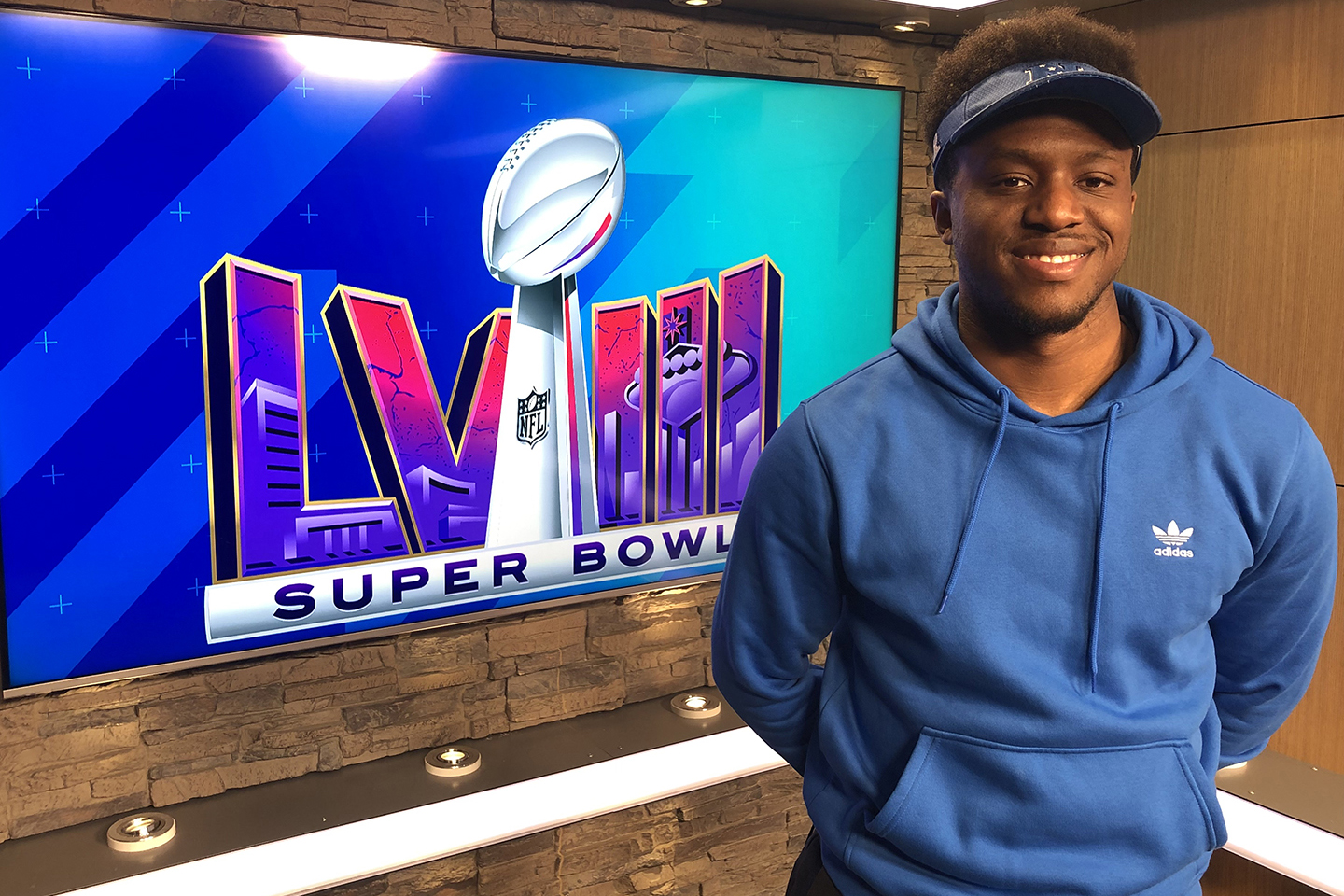 Student in blue sweatshirt standing in front of a TV monitor