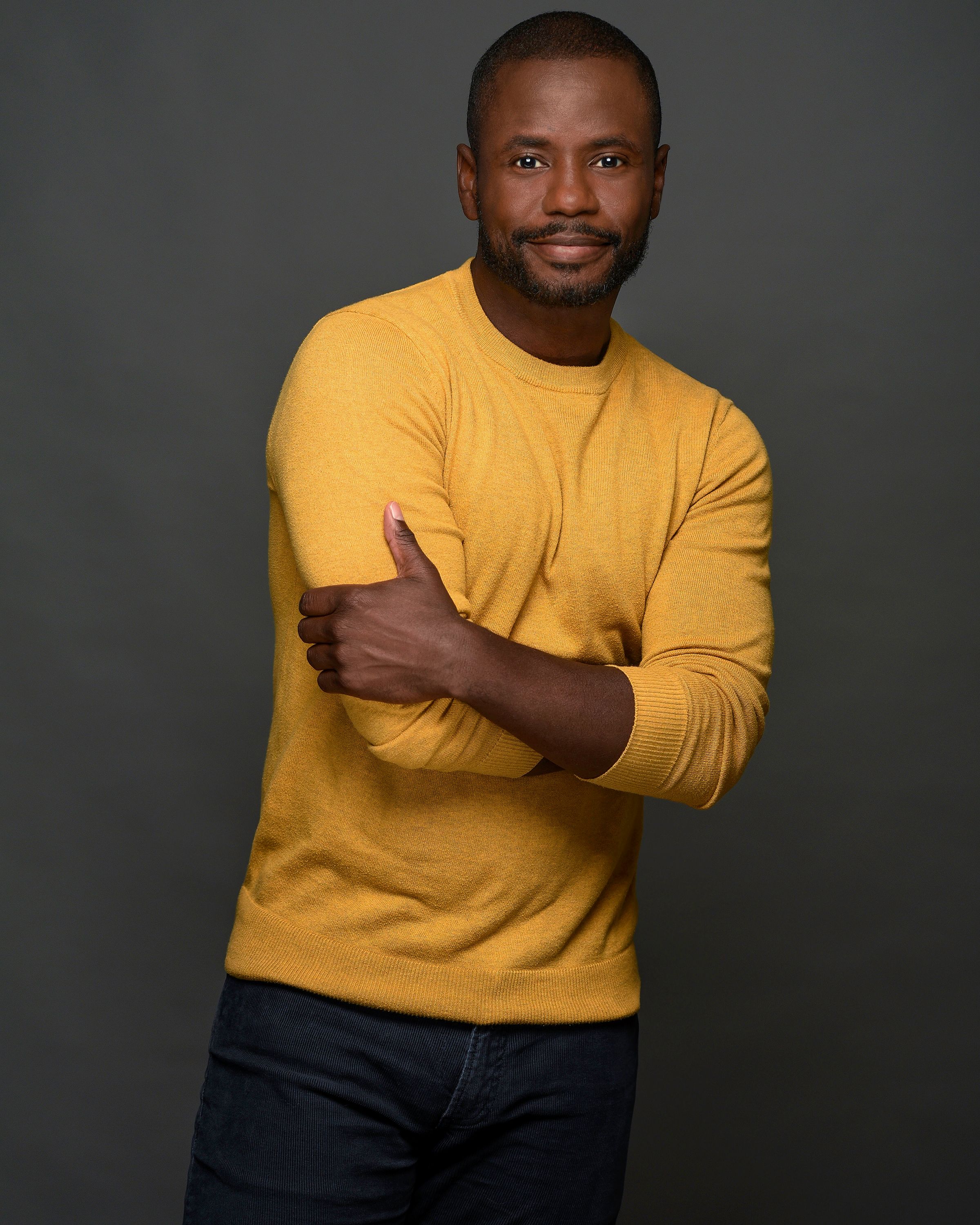 Black man with a yellow sweater posing casually