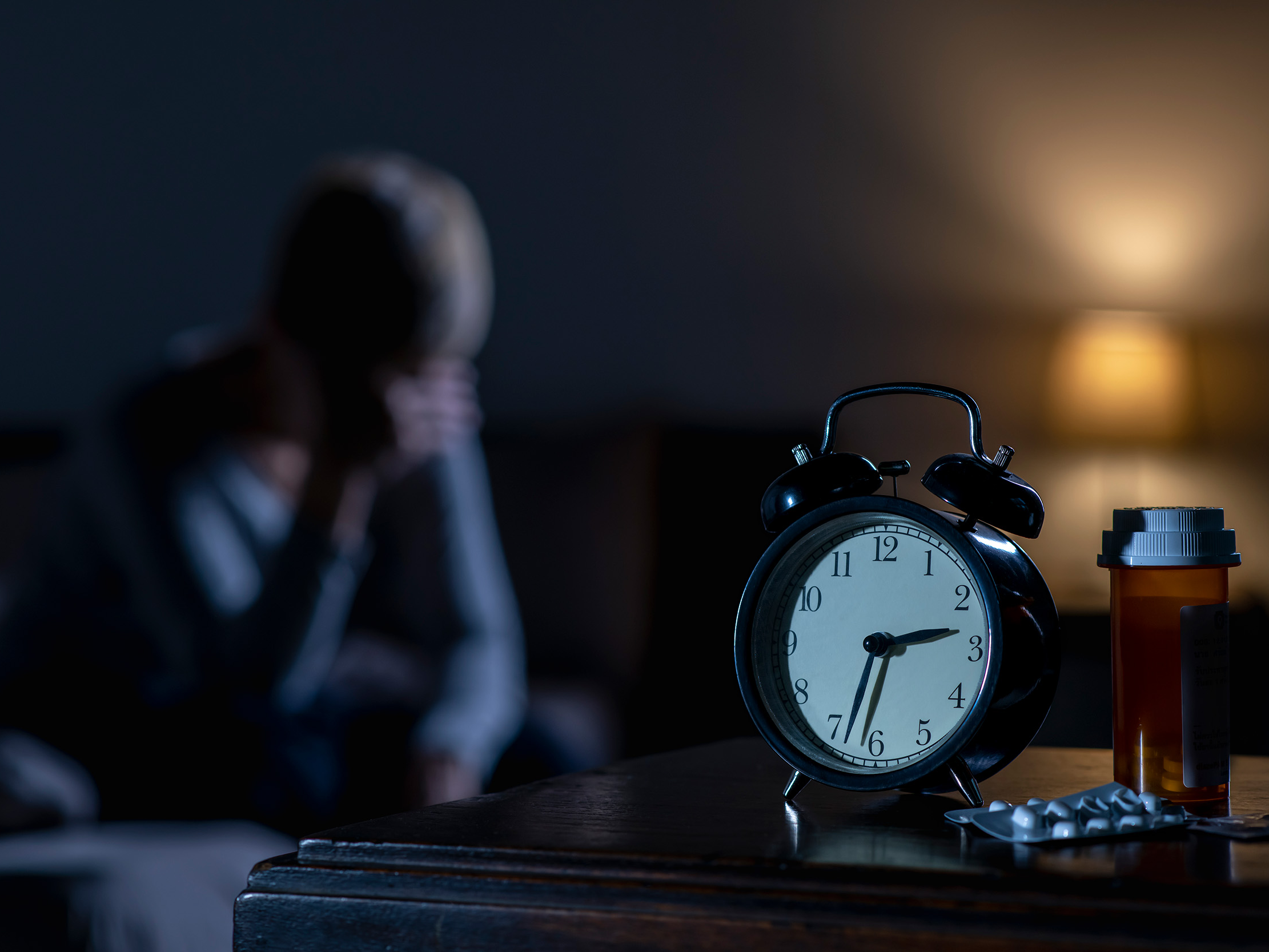 Alarm clock and pills with a person in the background