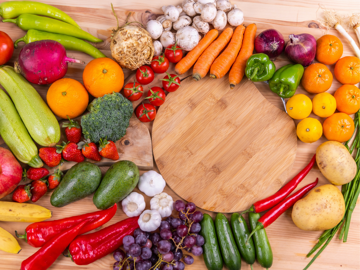 Fruits and veggies arranged on a table next to a cutting board