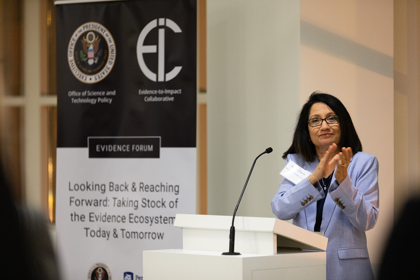 Penn State President Neeli Bendapudi applauds at a podium.