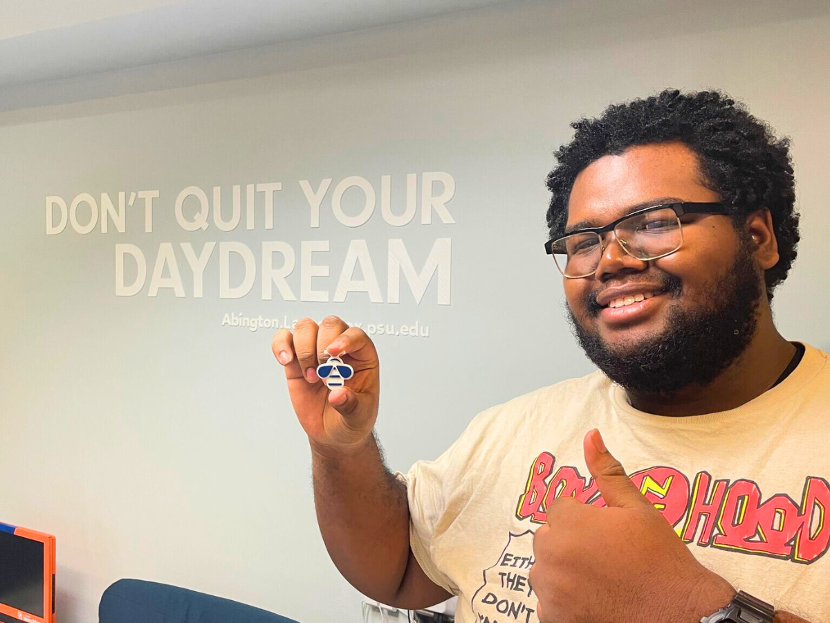 Darryl Gregory holds up a 3D print of a bee in front of a wall that says "Don't quit your daydream."