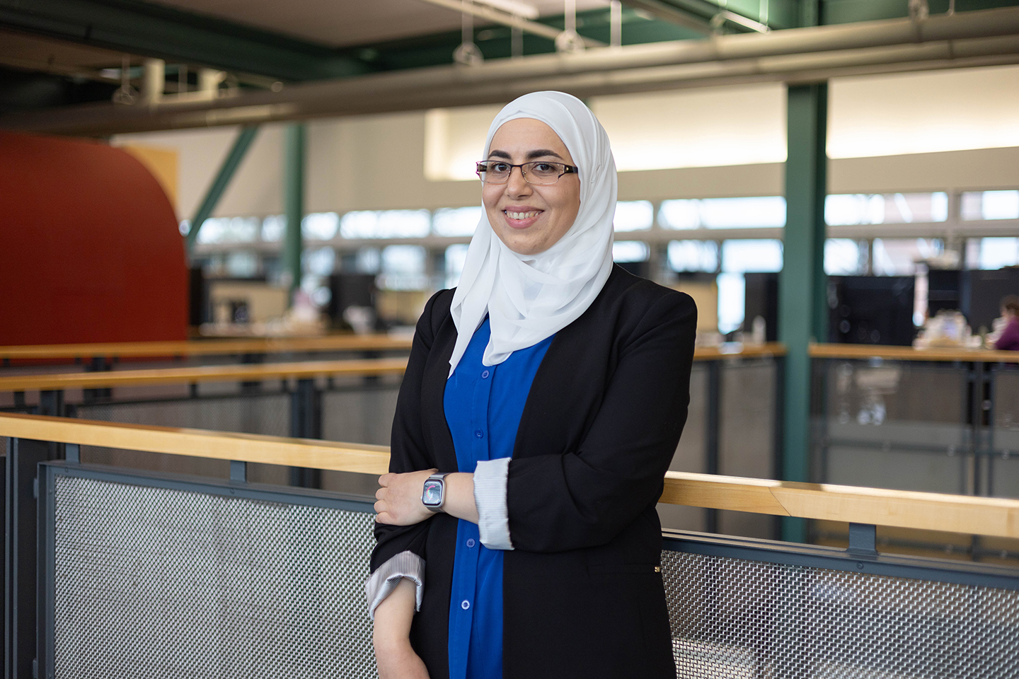 Dima Abu-Aridah in a white head scarf stands on the mezzanine level of the Stuckeman Family Building,