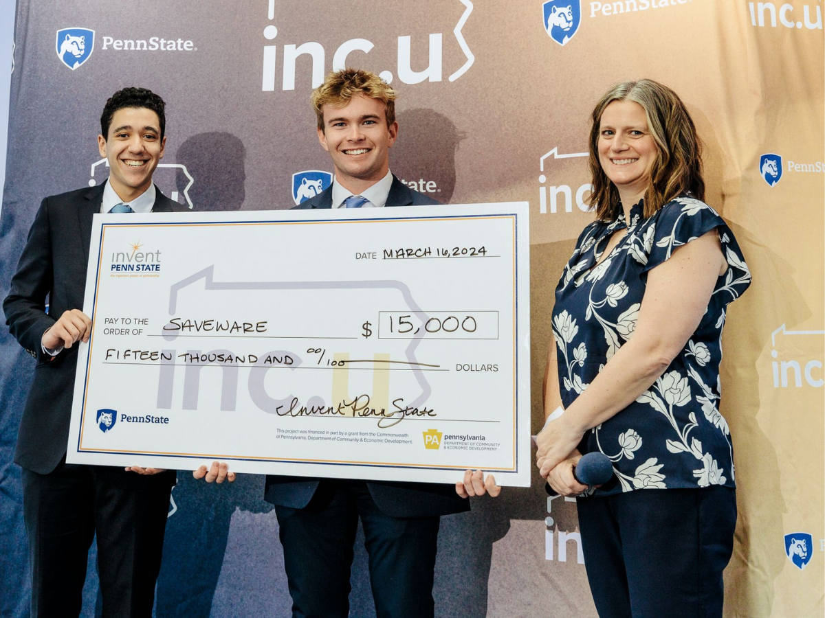 Staff member presenting oversized check for $15,000 to two students standing in front of Inc.U banner