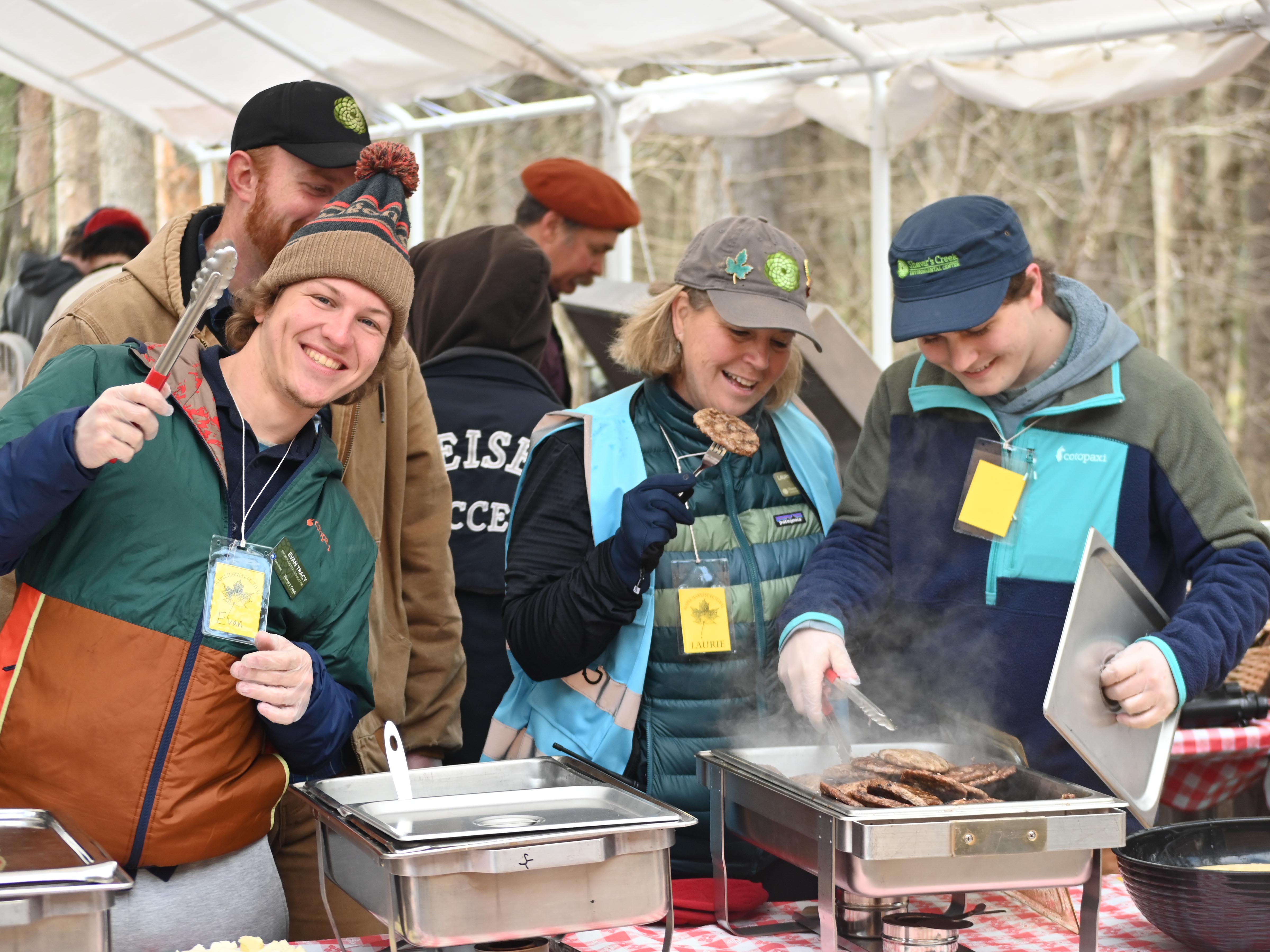 Three people serving sausage patties at Maple Harvest Festival