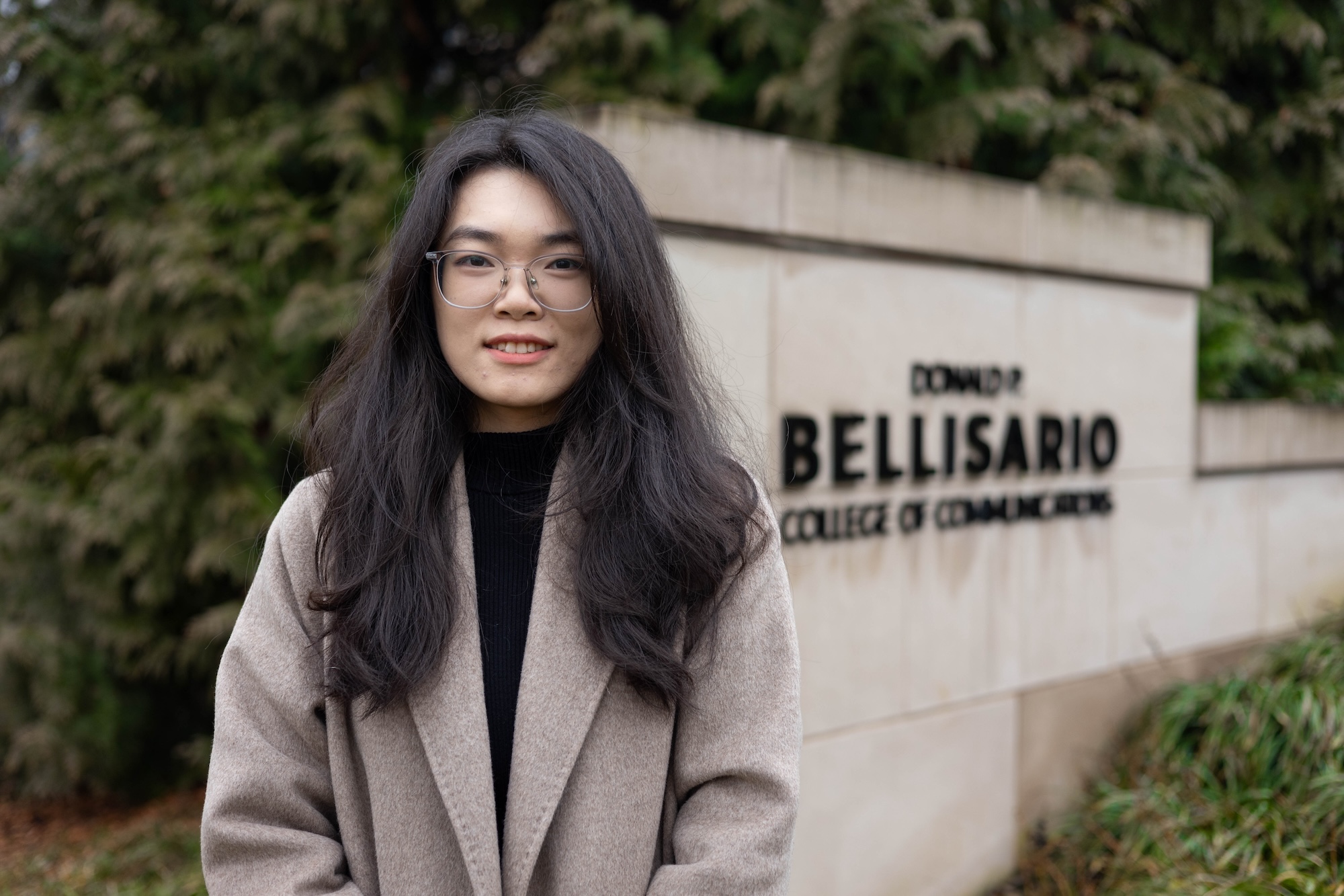 Maggie Liao standing outside Carnegie Building next to the sign for the Donald P. Bellisario College of Communications.