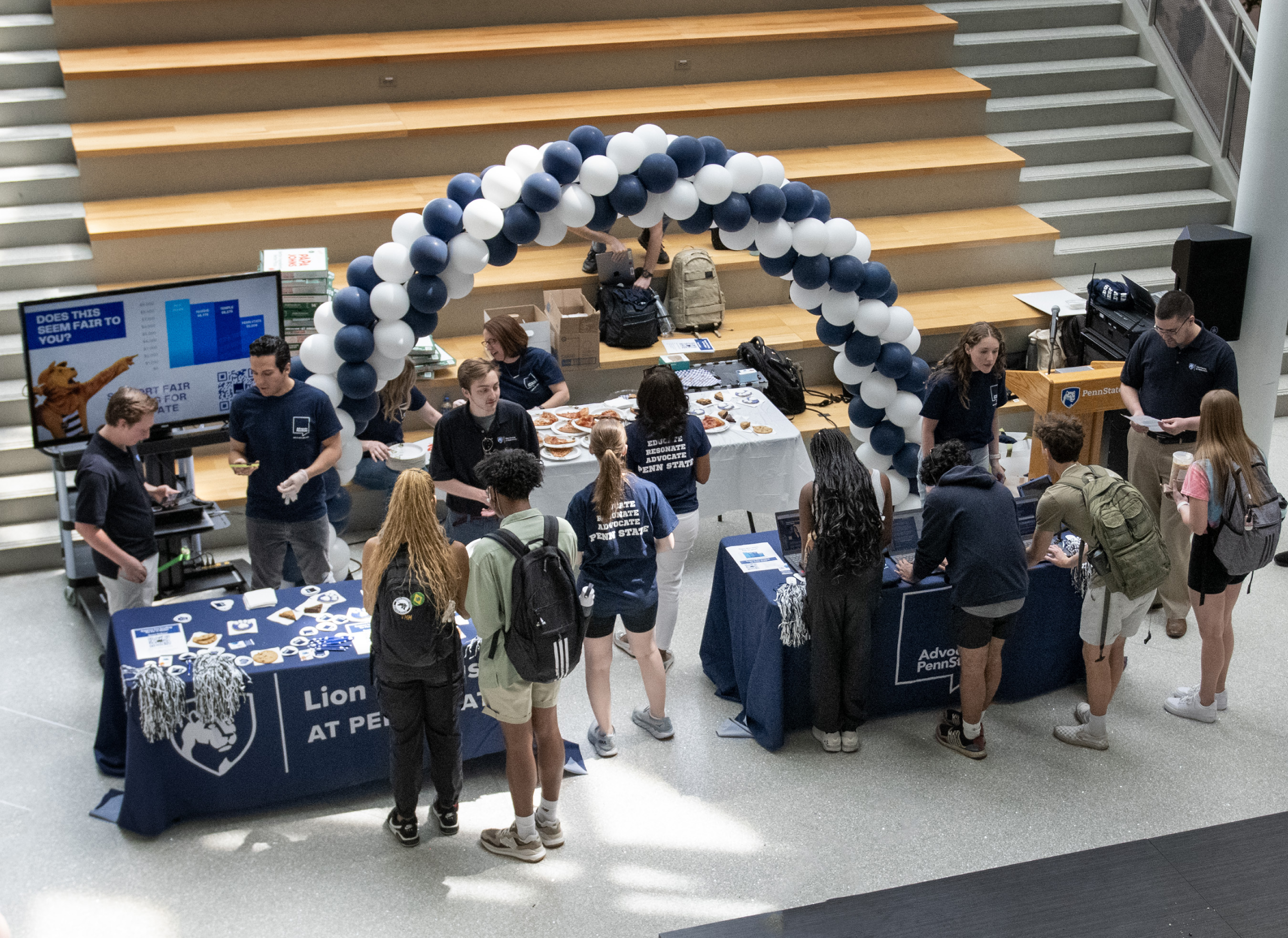 overhead shot of group of students and employees at two tables inside building in front of a large set of steps