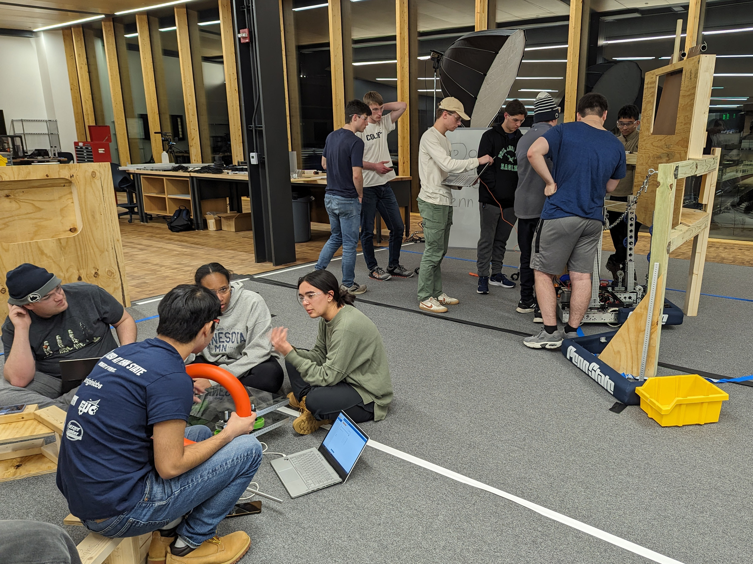 A group of students sits in the foreground talking, and a second group of students stands in the background, also collaborating.