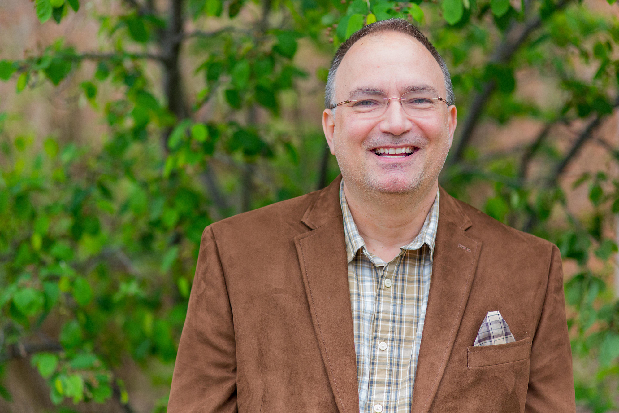 A photo of John Chapin wearing a brown jacket and smiling in a picture that was taken outdoors