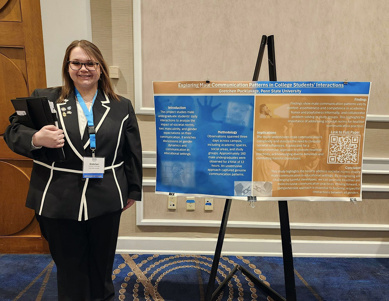 Female student holding folders and standing next to poster board positioned on an easel.